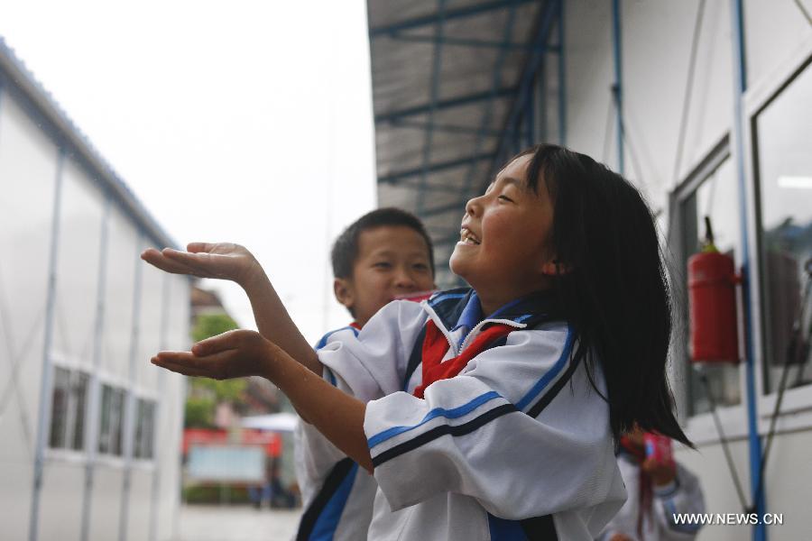 A student of the central primary school of Shangli Town enjoys the rain outside a makeshift classroom in Shangli, Lushan County, southwest China's Sichuan Province, May 16, 2013. The schoolhouses of the Shangli Town Center School were destroyed in the 7.0-magnitude earthquake taken place in Lushan on April 20, leaving more than 1, 200 students to have classes in newly built prefab houses. (Xinhua/Liu Xiao) 