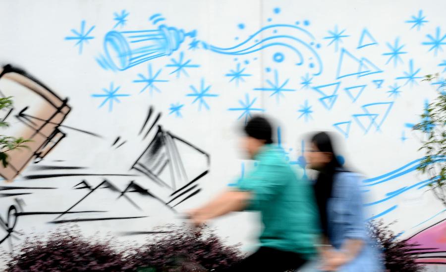 Citizens ride past a wall decorated with graffiti in Nanchang, capital of east China's Jiangxi Province, May 19, 2013. Two graduates from the Academy of Arts and Design in Hunan University of Science and Technology designed those graffiti to express their opinions of fashion. (Xinhua/Zhou Ke)