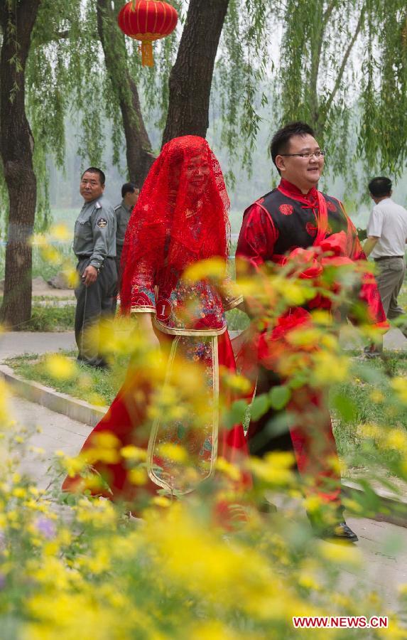 A groom and his bride walk during a group wedding held in the Old Summer Palace, or Yuanmingyuan park, in Beijing, China, May 18, 2013. A total of 30 couples of newlyweds took part in event with traditional Chinese style here on Saturday. (Xinhua/Luo Xiaoguang) 