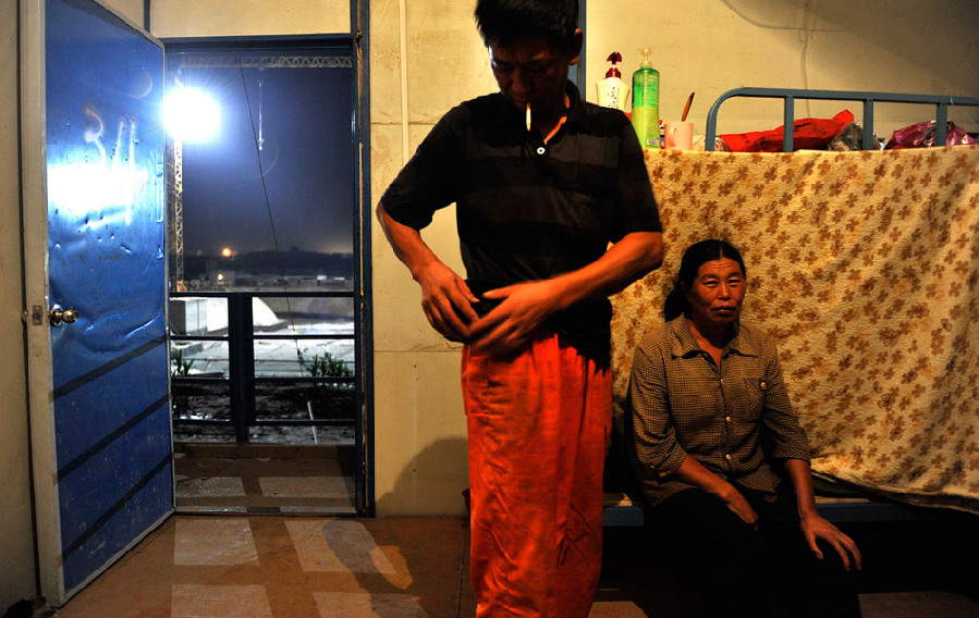 Weng Zhewu, 46, a migrant worker, just comes back from work and his wife sitting on the bed waits for him to go to bed together in Zhengzhou, Henan province. (Photo/ Guangming Online)