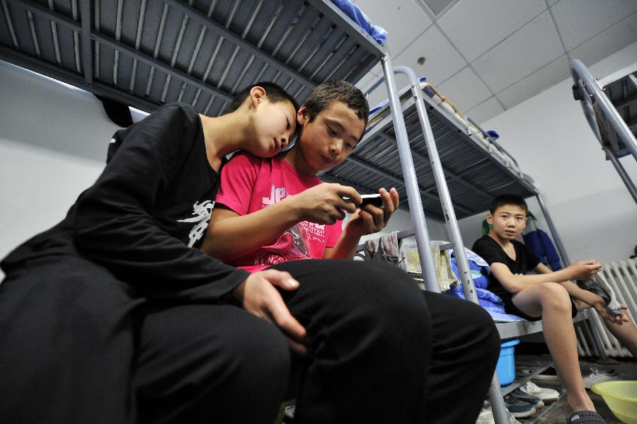Zhang Xiaoliang (C), a student of an acrobatics troupe, views his mobile phone with his roommate at their dorm in Yinchuan, capital of northwest China's Ningxia Hui Autonomous Region, May 20, 2013. Established in 1958, the acrobatics troupe was now affiliated with Ningxia Yinchuan Art Theatre. During the past few years, over 30 children between 5 and 13 years old have been admitted to the troupe to exercise acrobatics. In order to perform well on the stage, they exert much effort on exercising. Besides, they also learn general courses such as maths, Chinese and English. Yao Xing, deputy principal of the troupe, said that acrobatics requires painstaking effort, which will pay off one day. (Xinhua/Peng Zhaozhi)