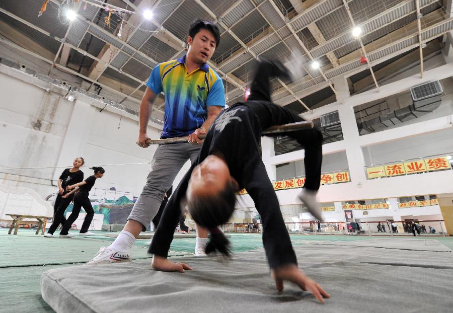 Yao Xing, deputy principal of an acrobatics troupe, helps students exercise at a training area in Yinchuan, capital of northwest China's Ningxia Hui Autonomous Region, May 20, 2013. Established in 1958, the acrobatics troupe was now affiliated with Ningxia Yinchuan Art Theatre. During the past few years, over 30 children between 5 and 13 years old have been admitted to the troupe to exercise acrobatics. In order to perform well on the stage, they exert much effort on exercising. Besides, they also learn general courses such as maths, Chinese and English. Yao Xing, deputy principal of the troupe, said that acrobatics requires painstaking effort, which will pay off one day. (Xinhua/Peng Zhaozhi)