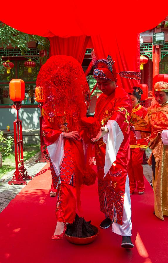 Bridegroom Zhang Lan (R) guides his Russian bride Ren Niya (her Chinese name) to walk past the Huopen, a fire pan as a symbol to bring good luck in traditional Chinese wedding, during the wedding ceremony in a courtyard dwelling in Chongqing, southwest China, May 23, 2013. The wedding ceremony, held in the traditional Chinese way, attracted lots of passengers to give their blessings. (Xinhua/Chen Cheng) 