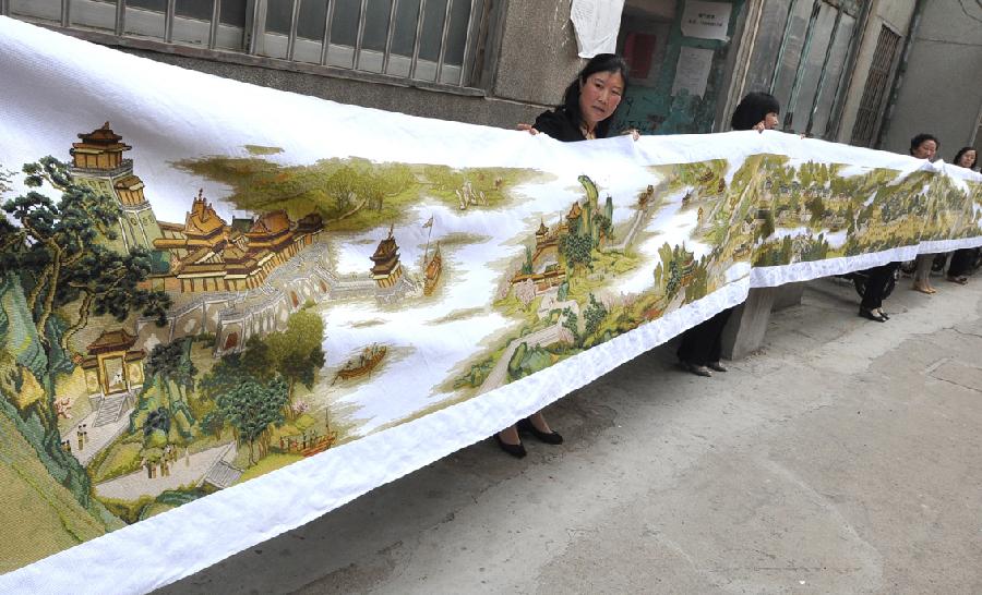 Yang Hua (L) demonstrates the 22-meter-long cross-stitch work of "Riverside Scene at the Qingming Festival" in Yiyuan County, east China's Shandong Province, May 22, 2013. Yang spent more than three years to finish the cross-stitch. (Xinhua/Zhao Dongshan)