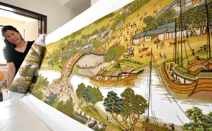 Yang Hua demonstrates the 22-meter-long cross-stitch work of "Riverside Scene at the Qingming Festival" in Yiyuan County, east China's Shandong Province, May 22, 2013. Yang spent more than three years to finish the cross-stitch. (Xinhua/Zhao Dongshan) 