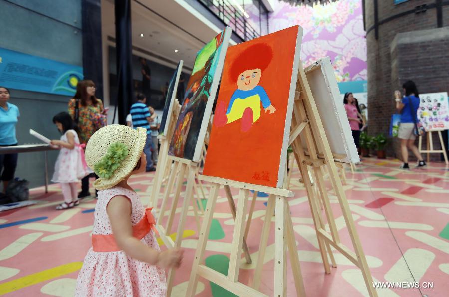 A child views paintings at a painting exhibition at the 798 art area in Beijing, capital of China, May 25, 2013. A two-day exhibition kicked off on Saturday, displaying paintings created by over 20 mentally retarded children from Chaoyang Anhua School. (Xinhua)
