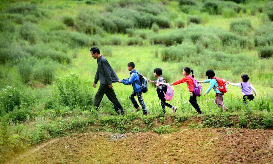 Wang Jiafu, 55, the only teacher in Tawan village, walks with his students to the classroom on the morning of May 17, 2013. Schools have been merged due to insufficient teachers and students which made the road to school much tougher and further. (Xinhua Photo/ Zhou Ke)