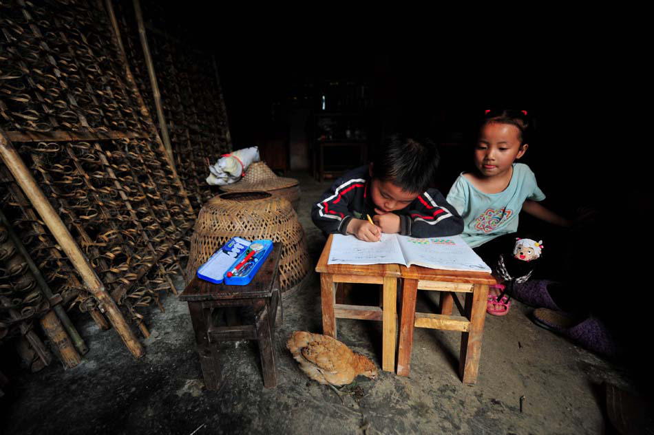 A girl watches a boy doing his homework in Guangxi's Changfeng county. Photo released by Xinhua News Agency on May 24, 2013. (Xinhua Photo/ Huang Xiaobang)