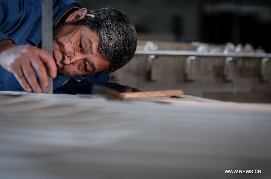 Photo taken on May 8, 2013 shows Zhang Gangning, a piano maker, measures fine differences between soundboards on a piano he makes in Nanjing, capital of east China's Jiangsu Province. (Xinhua/Yang Lei)