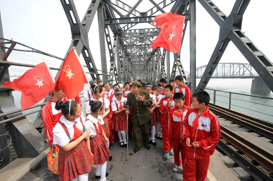 Veteran Sun Deli tells his story to students from Dandong Jiudao Elementary School on the China-DPRK Friendship Bridge in Dandong, northeast China's Liaoning Province, May 29, 2013. Various activities are held across China to celebrate the coming International Children's Day. (Xinhua/Yang Qing) 