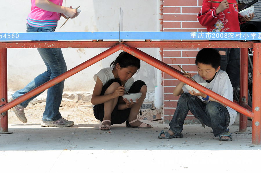 The students have meals in the shade of a table-tennis table at lunch time since there’s no cafeteria at school. (Photo by Huang Junhui/ cq.xinhuanet.com)