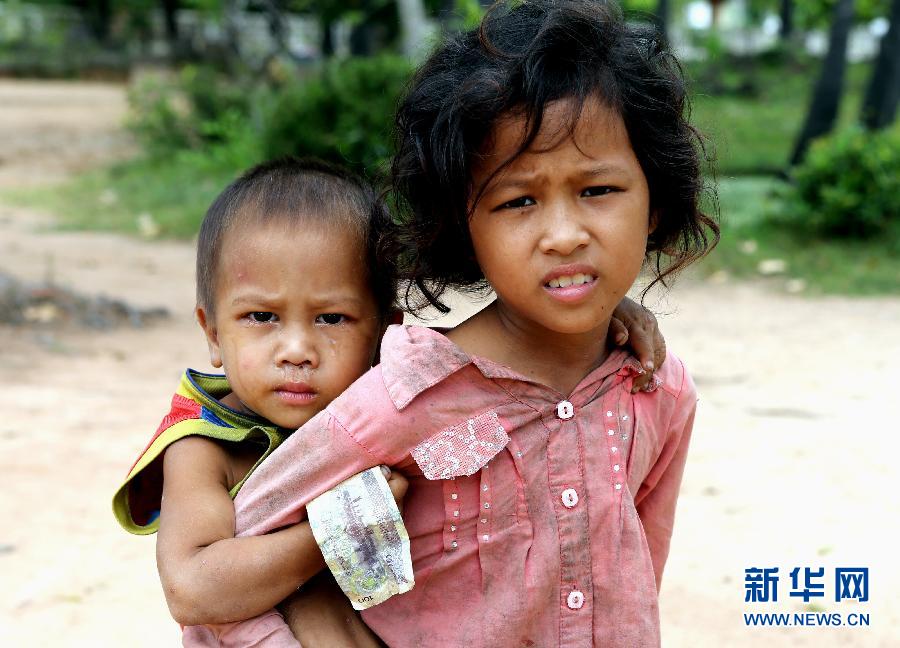 A girl carrying her younger brother begs tourists for money at Ta Prohm ruins, the outskirts of Phnom Penh, Cambodia. The girl quit school due to insufficient funds.  (Photo/Xinhua).