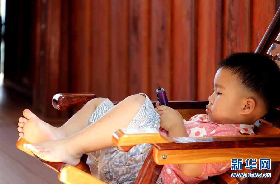 A child focus on his cell phone at a lake in Vientiane province, Laos, Nov. 7, 2012. (Photo/Xinhua)