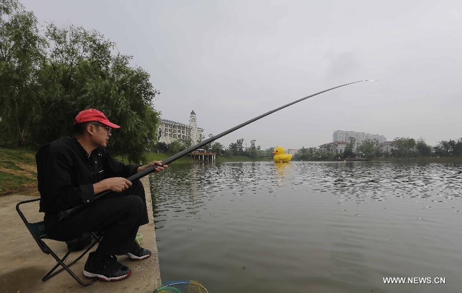 A man fishes near a mini rubber duck floating on a lake in the Hannan District of Wuhan, capital of central China's Hubei Province, June 1, 2013. The duck, made by a property company, is a mini copy of the huge rubber duck which appeared in Hong Kong, south China, on May 2. (Xinhua) 