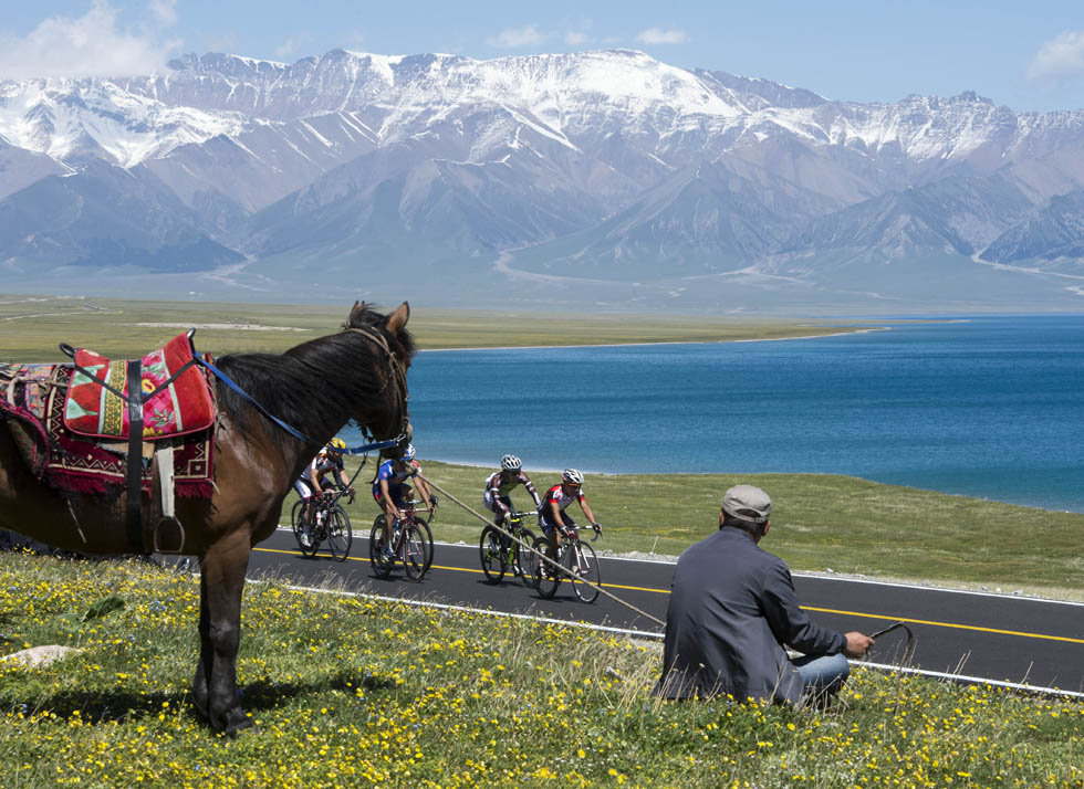 A herdsman watches cyclists competing in the Seventh Tour of Sailimu Lake Road Cycling Race in northwest China’s Xinjiang, May 31, 2013. (Xinhua/Jiang Wenyao)