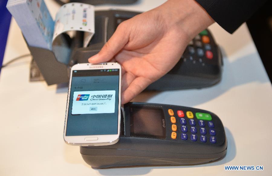 A staff member shows the payment method by using a mobile phone with mobile payment platform in Beijing, capital of China, June 9, 2013. China's UnionPay bank card network established the mobile payment platform with telecom operator China Mobile, according to a press conference on Sunday. (Xinhua/Li Xin)