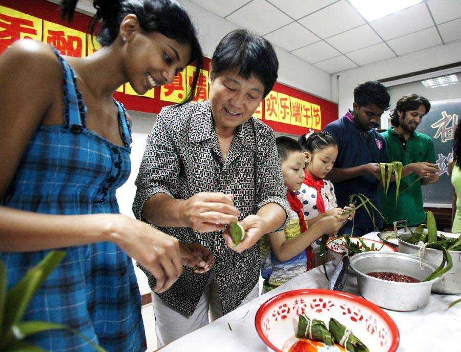 Foreign students of Tianjin Medical University join local residents in making zongzi, a pyramid-shaped dumpling made of glutinous rice wrapped in bamboo or reed leaves, to celebrate the upcoming Dragon Boat (Duanwu) Festival in Tianjin, north China, June 9, 2013. The Duanwu Festival falls on the fifth day of the fifth month in the Chinese lunar calendar, or June 12 this year. (Xinhua/Liu Dongyue)