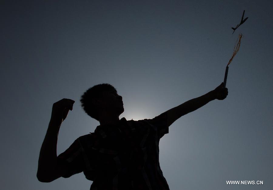 A student is silhouetted as he setting off a model aeroplane in southwest China's Chongqing Municipality, June 16, 2013. A competition for aeroplane model making was held here on June 16, attracting some 100 students from six nearby universities and colleges. (Xinhua/Chen Cheng)
