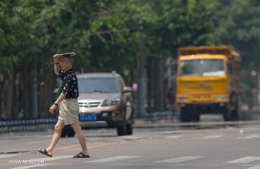 A man holds a fan as a shelter while walking on a street in southwest China's Chongqing Municipality, June 17, 2013. The highest temperature in Chongqing reached 39 degrees centigrade here on Monday. (Xinhua/Chen Cheng)