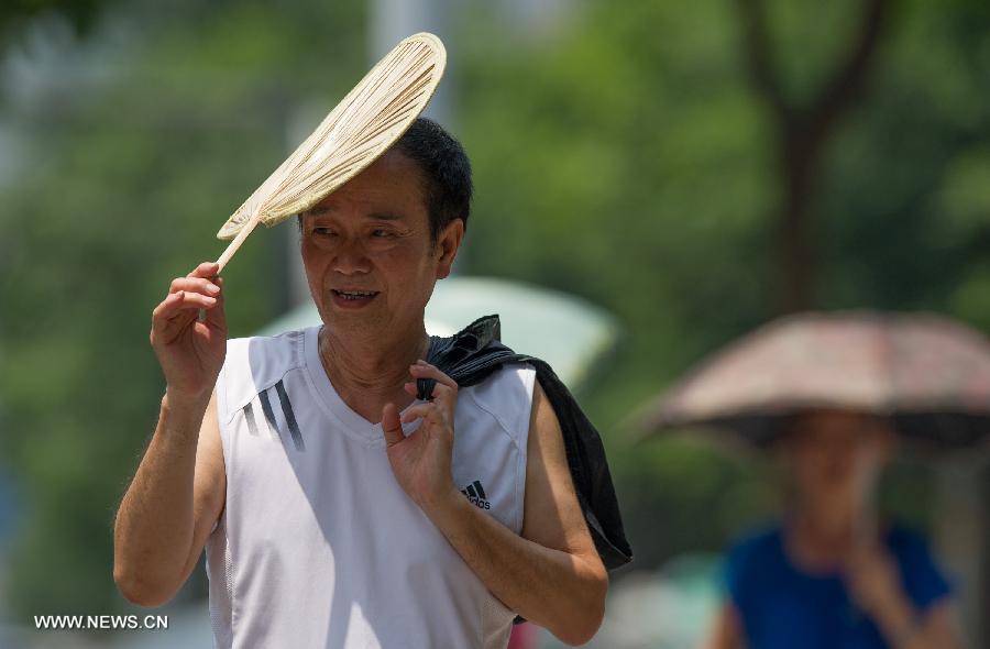 A man holds a fan as a shelter while walking on a street in southwest China's Chongqing Municipality, June 17, 2013. The highest temperature in Chongqing reached 39 degrees centigrade here on Monday. (Xinhua/Chen Cheng) 