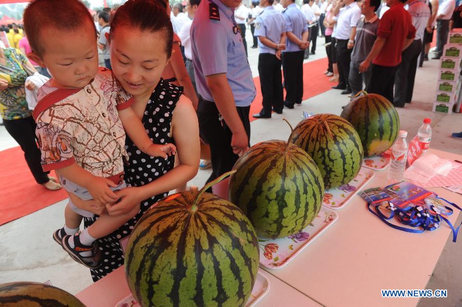 A woman carrying her son takes a look at the watermelons displayed during a watermelon festival in Fucheng County, north China's Hebei Province, June 18, 2013. The Fucheng County is a well-known watermelon growing area in north China, which grows 119,000 mu (about 8,000 hectares) watermelons and produces 550,000 tonnes of watermelons annually, with the annual sales volume reaching about 1 billion yuan (163.2 million U.S. dollars). (Xinhua/Wang Min)