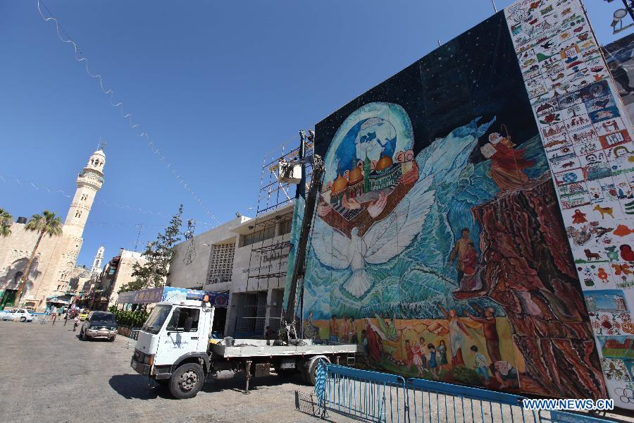 Palestinian workers are hanging the biggest oil painting in the world by the Palestinian artist Jamal Badwan near the Church of Nativity in the West Bank city of Bethlehem on June 19, 2013. The 310-square-meter painting portrait entered the Guinness Book of World Records. Jamal Badwan painted the earth surrounded by people of all ethnicities, panicking as a huge flood approaches. They are led to safety by a dove through Al-Aqsa Mosque, the Church of the Holy Sepulcher and a famous Kiev church. (Xinhua/Luay Sababa) 