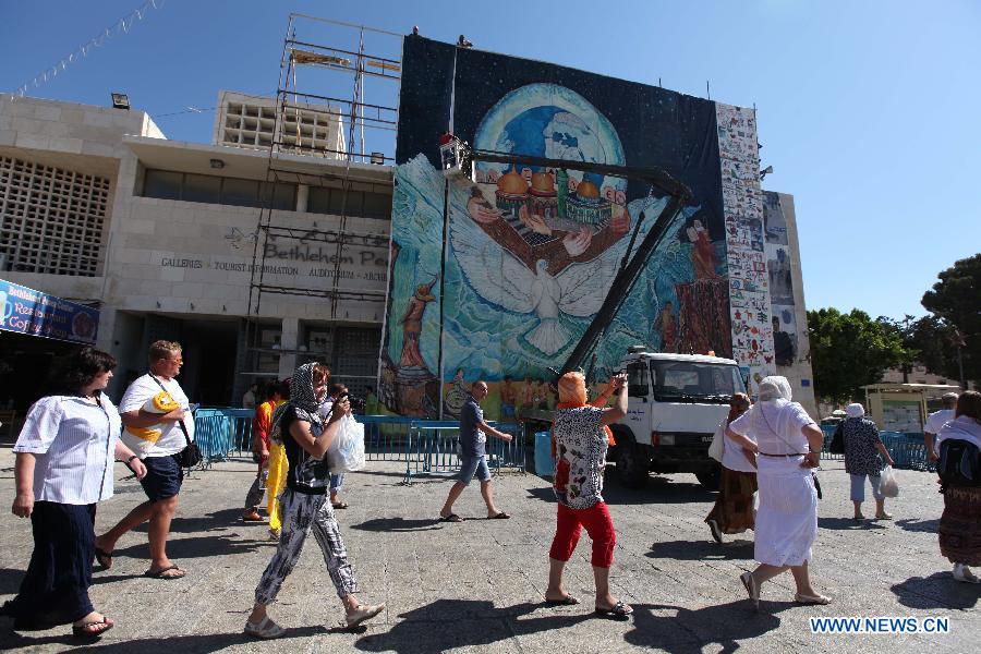 Palestinian workers are hanging the biggest oil painting in the world by the Palestinian artist Jamal Badwan near the Church of Nativity in the West Bank city of Bethlehem on June 19, 2013. The 310-square-meter painting portrait entered the Guinness Book of World Records. Jamal Badwan painted the earth surrounded by people of all ethnicities, panicking as a huge flood approaches. They are led to safety by a dove through Al-Aqsa Mosque, the Church of the Holy Sepulcher and a famous Kiev church. (Xinhua/Luay Sababa) 