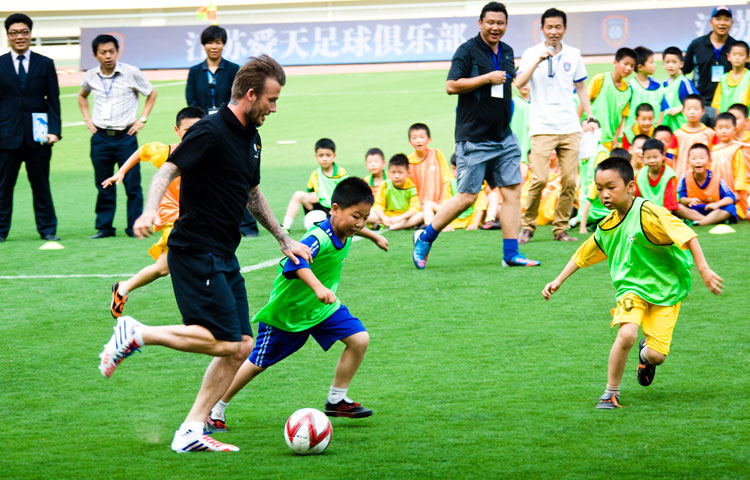 Become kid king: Recently retired football player David Beckham takes part in a training session with students at Nanjing Olympic Center in Nanjing, east China's Jiangsu Province, June 18, 2013. Beckham is on a seven-day visit to China as the ambassador for the Football Programme in China and China's Super League. (Photo/Osports)