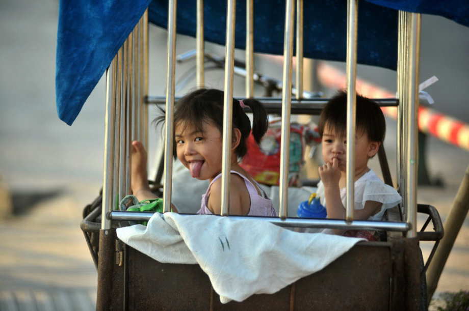 The two little girls are locked in a cage-like tricycle on the roadside of Binjiang Xilu in S China’s Guangxi on June 18, 2013.(Photo/ youth.cn)