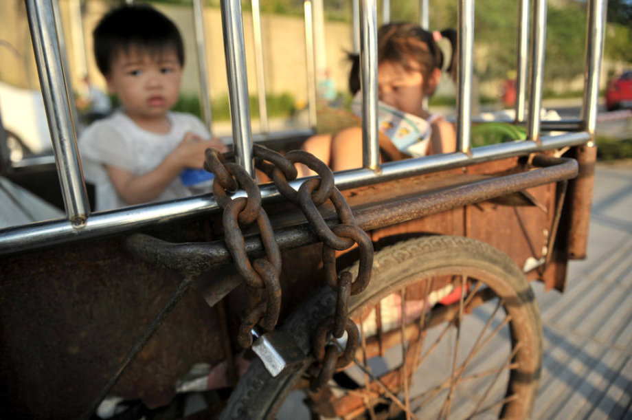 The two little girls are locked in a cage-like tricycle on the roadside of Binjiang Xilu in S China’s Guangxi on June 18, 2013.(Photo/ youth.cn)
