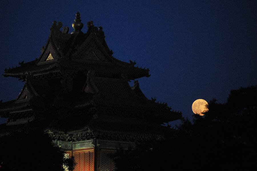 A full moon sets behind a building of the Forbidden City in Beijing, capital of China, June 23, 2013. The moon looks 14 percent larger and 30 percent brighter than usual on Sunday. The scientific term for the phenomenon is "perigee moon", but it is also known as a "super moon". (Xinhua/Sun Ruibo)