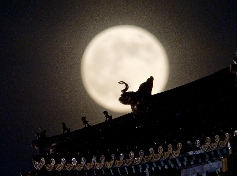 A full moon sets behind a building of the Forbidden City in Beijing, capital of China, June 23, 2013. The moon looks 14 percent larger and 30 percent brighter than usual on Sunday. The scientific term for the phenomenon is "perigee moon", but it is also known as a "super moon". (Xinhua/Chen Duo) 