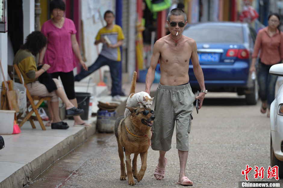 Xu Jin, 42, walks with his pets, a dog and a cat on a street in Kunming, Yunnan province June 23, 2013. The dog carries the cat on its back which made several pedestrians stop to take photos of the couple. (Photo by Liu Ranyang/ Chinanews.com)