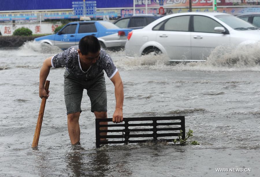 A pedestrian opens a sewer cover to drain off water as heavy rainfall hit Tongling of east China's Anhui Province, June 24, 2013. (Xinhua/Guo Shining)