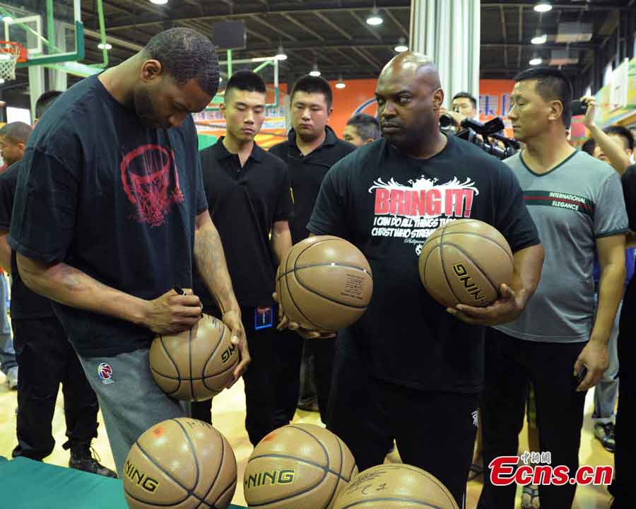 Tracy McGrady (L) autographs a basketball on a basketball court at the Jin Qiang national basketball training base in Chengdu, Southwest China's Sichuan Province, June 24, 2013. NBA stars visited Chengdu and played a game against China's August 1 Men's Basketball Team on Monday. (CNS/Liu Zhongjun)