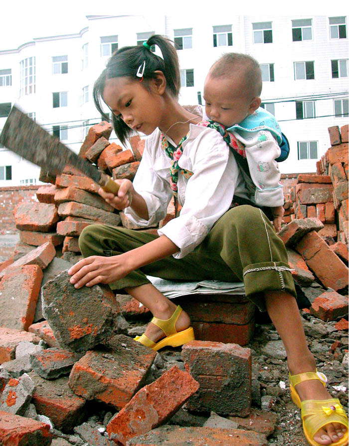 File photo taken on Aug. 6, 2002 shows that Zhao Hongyan, 9, picks up bricks to support the family, carrying her six-month-old brother on back at a construction site. Her story moved many and then she got sponsor to study at a vocational high school in 2011. After her graduation, Zhao was employed as a file clerk in Ningbo, Zhejiang province on June 21, 2013. (Photo by Gong Guorong/ Xinhua)