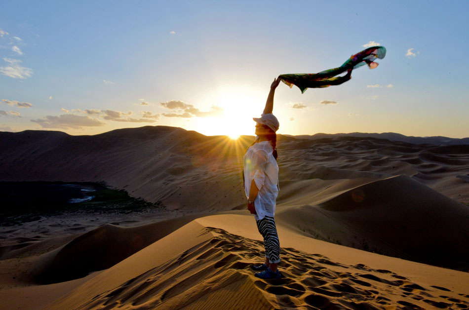 A tourist poses for photos in the Badain Jaran Desert, the third largest desert in China, which is located in Alxa right banner, west Inner Mongolia, June 18, 2013. The desert covers an area of 47,000 square kilometers, and contains Bilutu Peak – the world's highest stationary dune rising over 500 meters and peaking at 1,609 meters above sea level.  (Photo by Ren Junchuan/ Xinhua)