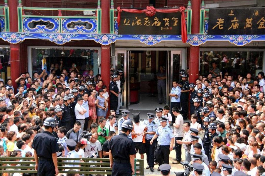 Policy officers arrest an armed robbery suspect at a gold shop in Tangyin, Henan province on Aug 2, 2012. Many people gathered outside the shop when they heard the news. (Photo/CNTV) 