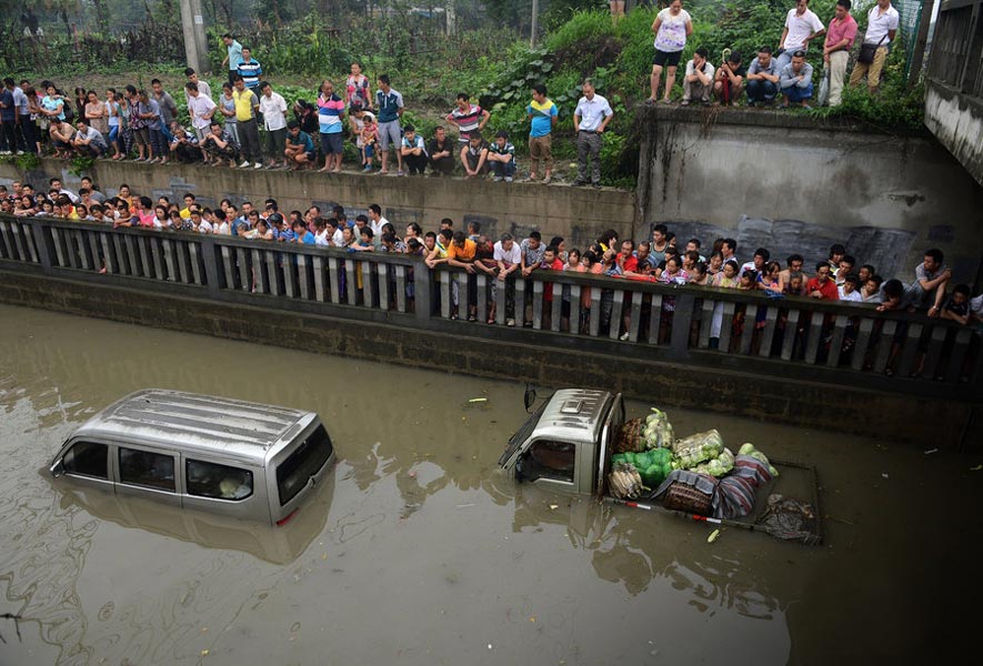 People gather together to look at an abandoned minivan submerged in the water on June 20, 2013. Rainstorm hit Chengdu on June 19, causing heavy flood in the city. (Photo/CNTV)