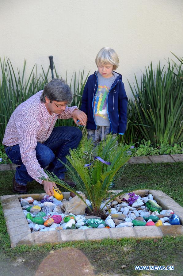 A father talks with his son beside colorful stones with best wishes for South Africa's anti-apartheid icon Nelson Mandela outside his residence in Johannesburg, South Africa, June 27, 2013. South African President Jacob Zuma has canceled his scheduled visit to Mozambique after visiting former president Nelson Mandela in hospital, the Presidency said Wednesday night. (Xinhua/Guo Xinghua)