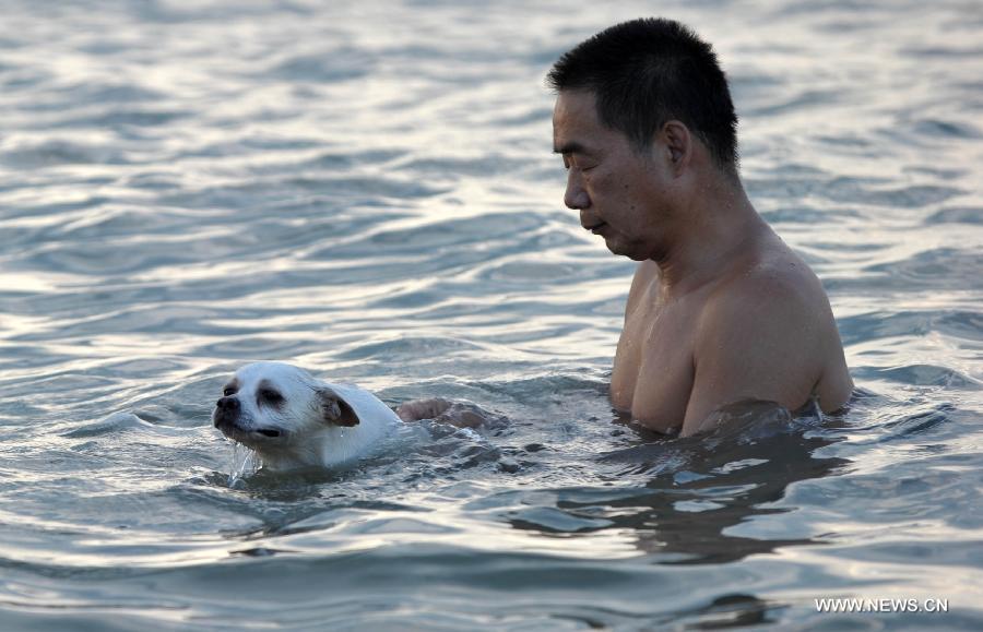 A man plays with his dog in the sea near Haikou, capital of south China's Hainan Province, June 29, 2013. The highest temperature in Haikou reached 35 degree centigrade, driving local residents to the seashore. (Xinhua/Zhao Yingquan)