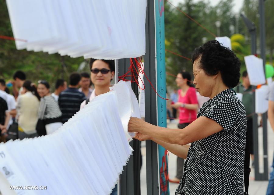 A parent reads personal information of people attending a blind date party at a park in Changchun, capital of northeast China's Jilin Province, June 30, 2013. (Xinhua/Xu Chang)