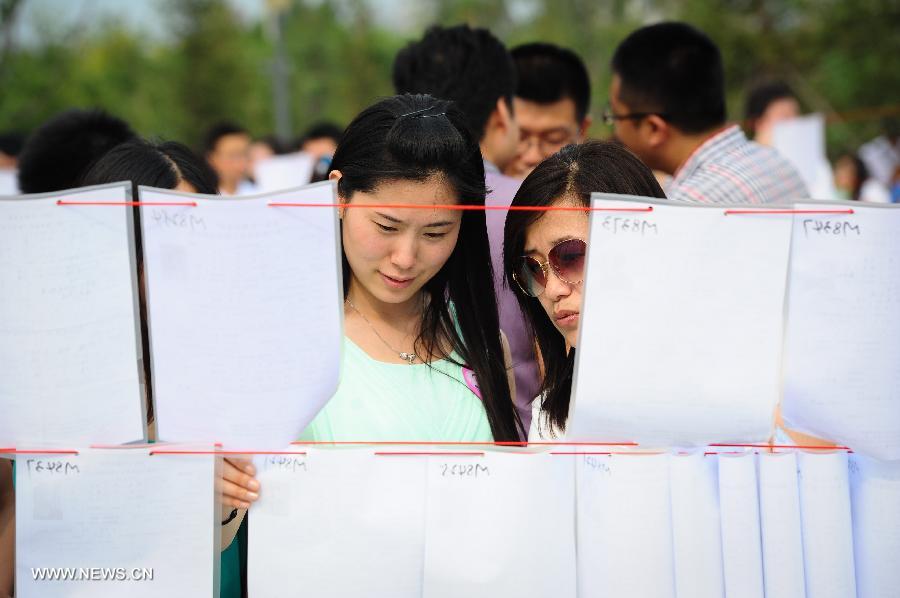 Two women read personal information of people attending a blind date party at a park in Changchun, capital of northeast China's Jilin Province, June 30, 2013. (Xinhua/Xu Chang)