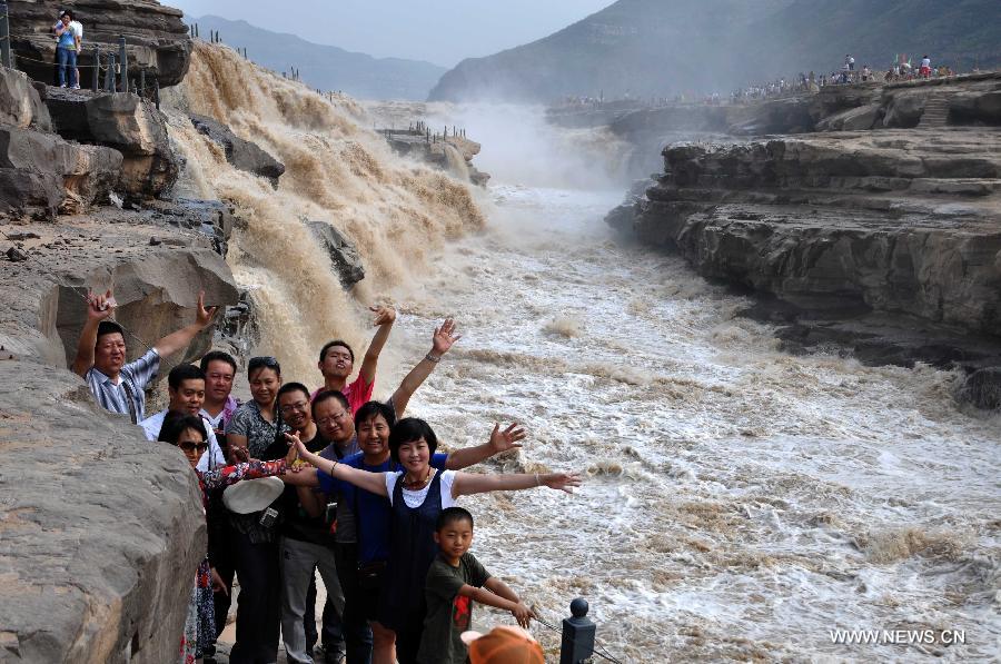 People pose for photos in front of the Hukou Waterfall of the Yellow River in Jixian County, north China's Shanxi Province, June 30, 2013. (Xinhua/Lv Guiming)