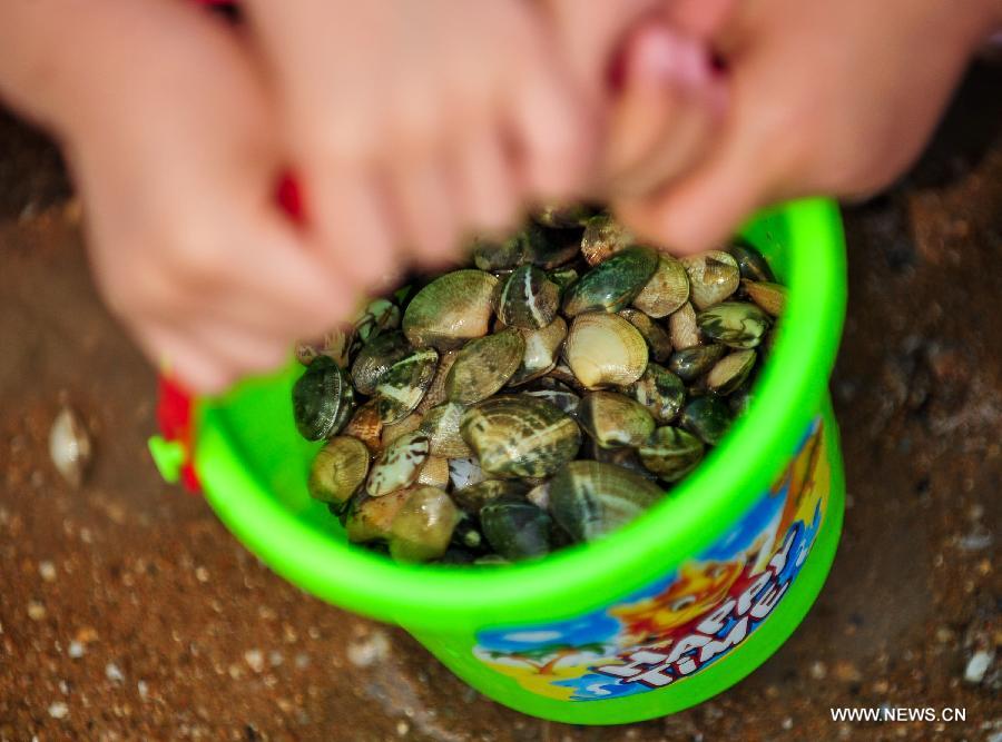 Children carry a bucket of shells on the bathing beach in Dongjiangwan of north China's Tianjin Municipality, June 30, 2013. Many people came to Dongjiangwan to spend their weekends. (Xinhua/Zhang Chaoqun)