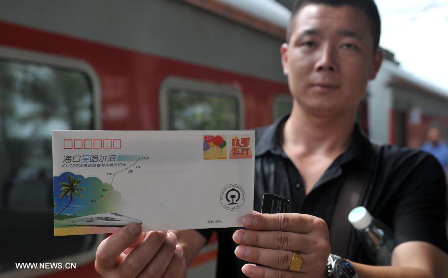 A passenger shows a souvenir envelope for the first direct train from Haikou to Harbin at the Haikou Railway Station in Haikou, capital of south China's Hainan Province, July 2, 2013. The train K1122/3 from south China's Haikou to northeast China's Heilongjiang left Haikou Tuesday, a day later than its original departure date due to the tropical storm Rumbia. The train which travels 4,458 kilometers for 65 hours has connected China's southernmost capital city Haikou of Hainan Province with China's northernmost capital city Harbin of Heilongjiang Province. (Xinhua/Zhao Yingquan)