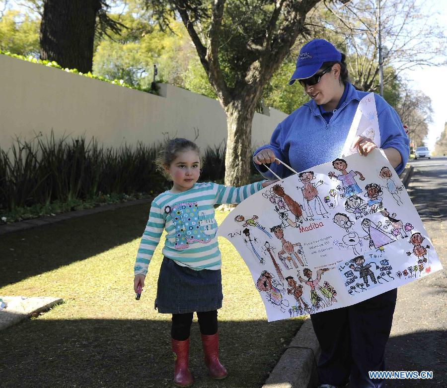 A woman and her daughter take a painting which drawn by the child and her friends to present to Nelson Mandela outside Mandela's house in Johannesburg, South Africa, on July 2, 2013. South Africans are ready to celebrate the 95th birthday of anti-apartheid icon Nelson Mandela who has been hospitalized for more than three weeks for a recurring lung infection, President Jacob Zuma said. Zuma said Mandela "is still critical but stable" in a Pretoria hospital where he was admitted on June 8. (Xinhua/Li Qihua)