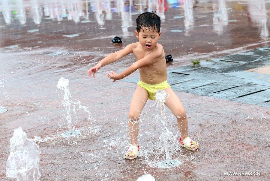 A boy plays with the water of a fountain on a square in central China's city Wuhan on June 29, 2013.  (Xinhua/Cheng Min)
