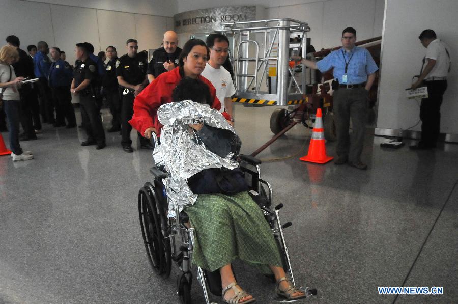 A passenger covering her face leaves the room where passengers from the crash-landed Asiana Airlines flight rest in at San Francisco International Airport, the United States, July 6, 2013. The South Korean consulate has confirmed that the pair killed in a crash landing of an Asiana Airlines plane at San Francisco airport were women holding Chinese passports, the Chinese Consulate General in San Francisco told Xinhua Sunday. (Xinhua/Liu Yilin)