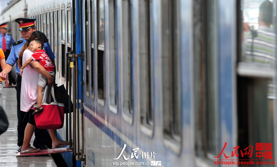 A child accompanied by adult takes the train to spend holidays with his parents working in city at Fuyang Railway Station, east China's Anhui province, July 1, 2013. (photo/vip.people.com.cn)